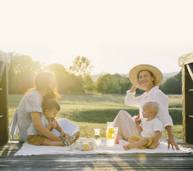 Lächelnde Frauen mit ihren Söhnen, die beim Picknick Zeit miteinander verbringen - NDEF00390