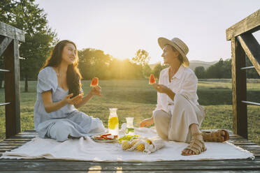 Happy women holding slices of watermelon sitting on picnic blanket - NDEF00391
