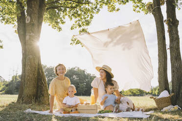 Glückliche Frauen sitzen mit ihren Söhnen auf einer Picknickdecke im Park - NDEF00412