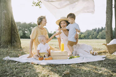 Glückliche Frauen genießen ein Picknick mit ihren Söhnen im Park - NDEF00413
