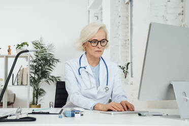 Älterer Arzt bei der Arbeit an einem Desktop-PC in einer Klinik - VPIF07967