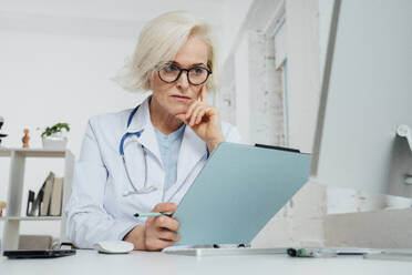 Älterer Arzt, der ein Dokument am Schreibtisch in einer Klinik untersucht - VPIF07970