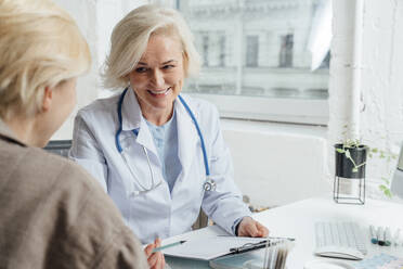 Smiling mature doctor discussing over document with patient - VPIF07977