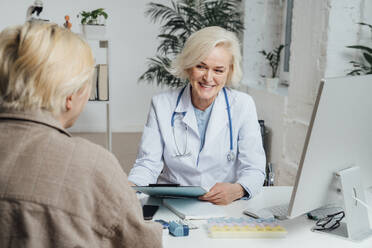 Smiling doctor discussing over document with patient - VPIF07978