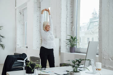 Smiling businesswoman stretching arms at office - VPIF08006