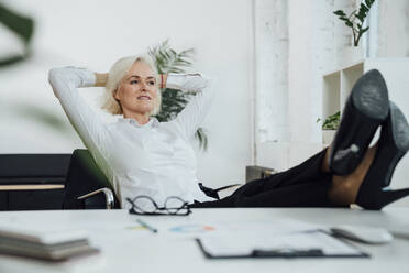 Smiling businesswoman with hands behind head sitting at desk - VPIF08007