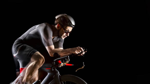 Cyclist sitting on turbo trainer against black background - STSF03698