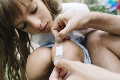 Vater legt Verband auf das Knie seiner Tochter - TYF00788