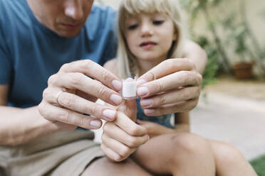 Vater legt Verband auf den Daumen seiner Tochter - TYF00789