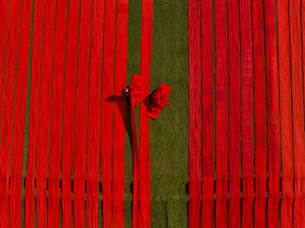 Luftaufnahme von Menschen, die auf einem Feld arbeiten und rote Baumwollstoffrollen in Narsingdi, Dhaka, Bangladesch, spannen. - AAEF17359