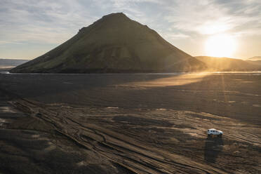 Luftaufnahme eines Fahrzeugs, das bei Sonnenuntergang den Berg Maelifell entlang fährt, Island. - AAEF17391