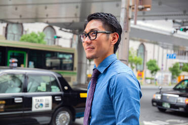 Ein junger Geschäftsmann in der Stadt, unterwegs, ein Mann in blauem Hemd und Krawatte, ein Taxi hinter ihm. - MINF16596