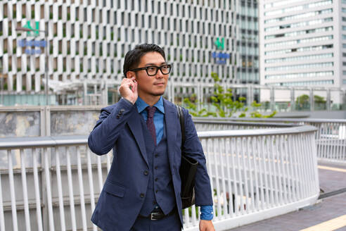 Ein junger Geschäftsmann in blauem Jackett, Hemd und Krawatte steht auf einem Gehweg in der Innenstadt. - MINF16605