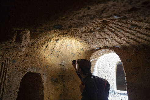 Tourist erkundet etruskische Nekropole von San Guilano mit Smartphone-Taschenlampe - MAMF02636