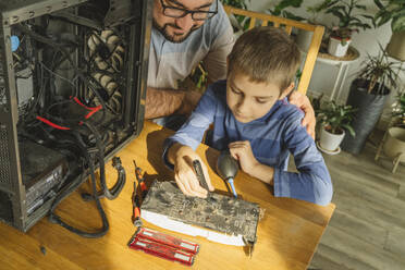 Son repairing motherboard on table by father at home - OSF01438