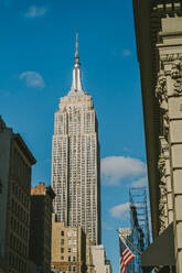 Von unten der amerikanischen Flagge neben dem Empire State Building in New York City gegen den blauen Himmel - ADSF43244