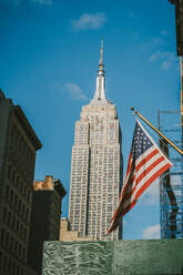 Von unten der amerikanischen Flagge neben dem Empire State Building in New York City gegen den blauen Himmel - ADSF43245