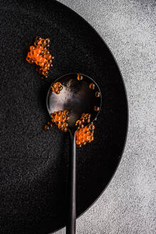 Black spoon full of red caviar on black plate and same color stone concrete table background - ADSF43283