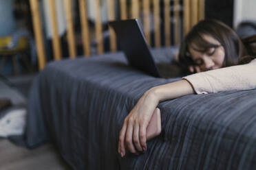 Müde junge Frau mit Smartphone auf dem Bett liegend zu Hause - ANNF00045