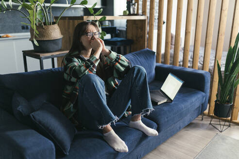 Depressive junge Frau sitzt zu Hause auf dem Sofa - ANNF00073
