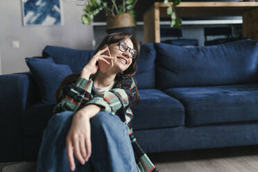 Glückliche junge Frau, die zu Hause sitzt und mit ihrem Handy spricht - ANNF00080