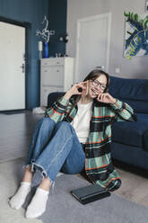 Happy woman wearing eyeglasses talking on smart phone sitting at home - ANNF00081