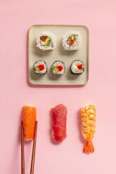 Flat Lay von verschiedenen Sushi-Rollen auf Platten mit Stäbchen und Sojasauce auf rosa Hintergrund platziert - ADSF43354