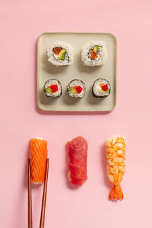 Flat Lay von verschiedenen Sushi-Rollen auf Platten mit Stäbchen und Sojasauce auf rosa Hintergrund platziert - ADSF43354