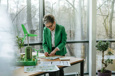 Mature businesswoman sketching blueprint at desk in office - YTF00610