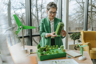 Smiling businesswoman holding biophilic architecture model in office - YTF00615