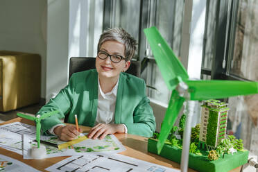 Smiling mature businesswoman sitting with blueprint in office - YTF00623