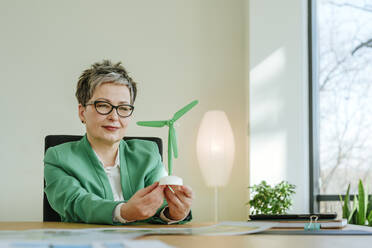 Mature businesswoman looking at wind turbine in office - YTF00638