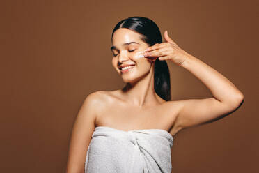 Schöne hispanische Frau, die ihre Haut mit einer feuchtigkeitsspendenden Lotion verwöhnt und es genießt, eine gesunde Hautpflegeroutine für einen strahlenden Teint zu praktizieren. - JLPSF29368
