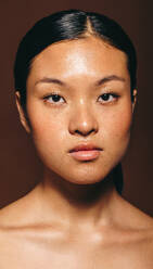 Eine schöne asiatische Frau mit strahlender Haut blickt selbstbewusst in die Kamera und zeigt die Ergebnisse einer konsequenten Hautpflege und fühlt sich durch ihr makelloses Aussehen gestärkt. - JLPSF29400