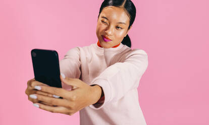 Eine selbstbewusste Gen Z-Frau zeigt ihren trendigen zweifarbigen Lippenstift, während sie ein stylisches Selfie mit ihrem Smartphone macht - JLPSF29458