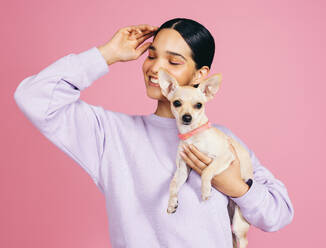 Happy young woman in her 20s smiling brightly as she cradles an adorable puppy in her arm. Youthful female beaming joy and positivity as she holds her tiny pet in a studio. - JLPSF29482