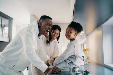 Eltern lachen fröhlich in der Küche mit ihrer kleinen Tochter. Mama und Papa machen glückliche Familienerinnerungen mit ihrem Kleinkind. Afrikanische Familie ist in der Küche und genießt einige Zeit zusammen. - JLPSF29505