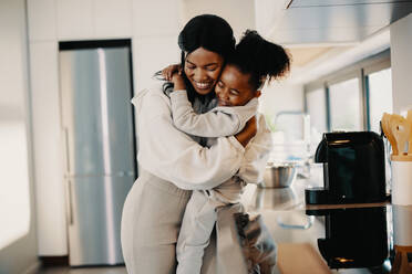 Ich liebe dich, Mama, kleines Mädchen umarmt ihre Mutter in der Küche. Mutter und Tochter feiern den Muttertag in passenden Outfits. Liebe zwischen einer Mutter und ihrem Kind. - JLPSF29521