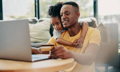 Online-Shopping und E-Commerce, Vater und Tochter kaufen einige Dinge online mit einer Kreditkarte. Mann und seine Tochter stöbern in einem Online-Shop auf einem Laptop. Vater verwöhnt sein Kind mit einigen Einkäufen. - JLPSF29540