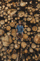 Man sitting on stack of logs in lumberyard - PCLF00254