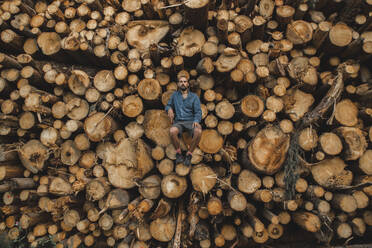 Man sitting on pile of logs at lumberyard - PCLF00255