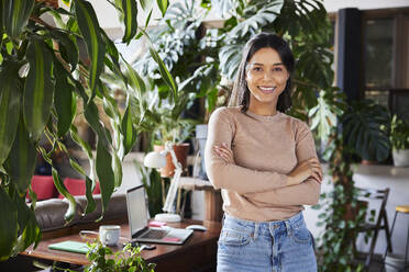 Confident businesswoman with arms crossed standing at loft office - BSZF02272