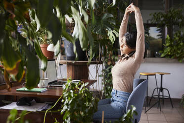 Tired businesswoman stretching after work at loft office - BSZF02276