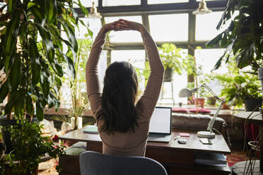 Businesswoman stretching at desk in loft office - BSZF02277