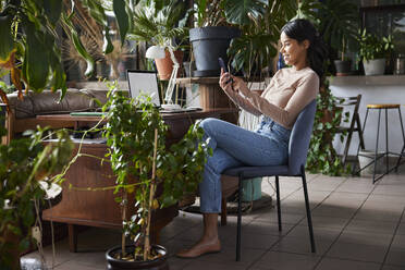 Smiling businesswoman surfing net through smart phone at loft office - BSZF02278