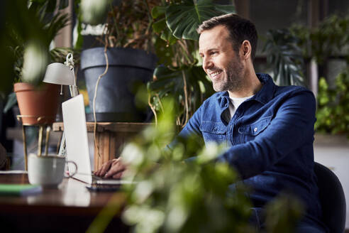 Happy businessman using laptop at loft office - BSZF02285