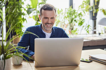 Smiling businessman using laptop at loft office - BSZF02290