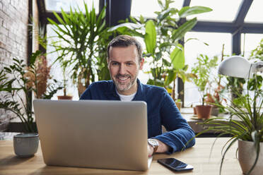 Businessman working on laptop at desk in loft office - BSZF02292