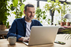 Businessman surfing net on laptop at loft office - BSZF02293