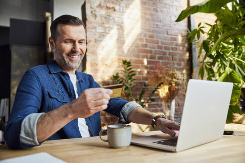 Lächelnder Geschäftsmann beim Online-Banking mit Kreditkarte im Loft-Büro - BSZF02314